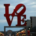 LOVE art sign in Philadelphia's Love Park / JFK Plaza at dusk with streetlights and buildings visible in background.